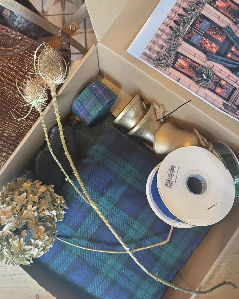 Installation planning box with tartan fabric and ribbon, brass bells, dried teasels and hydrangea, and a mood board photo of a shopfront garland