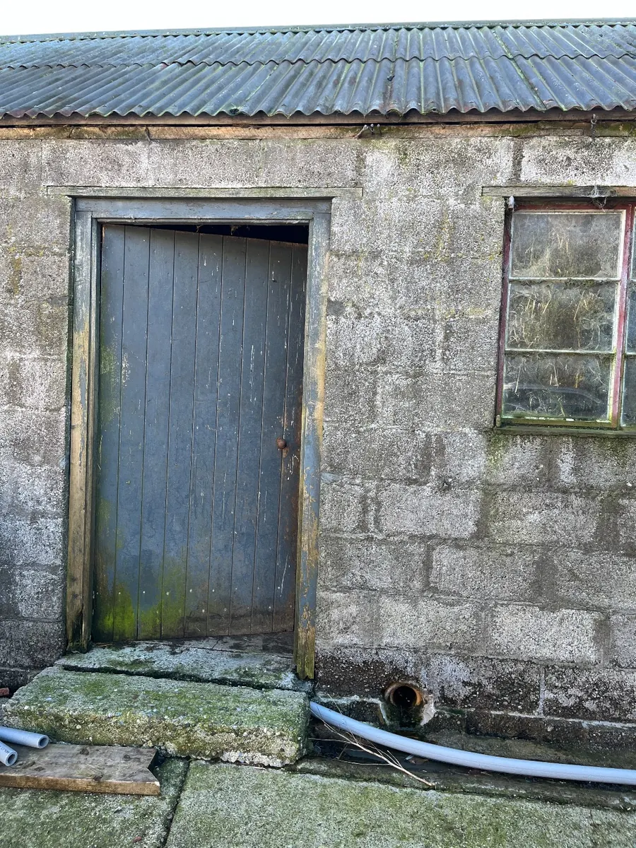 The old calf shed before work began, with a weathered blue-grey door and cracked block walls
