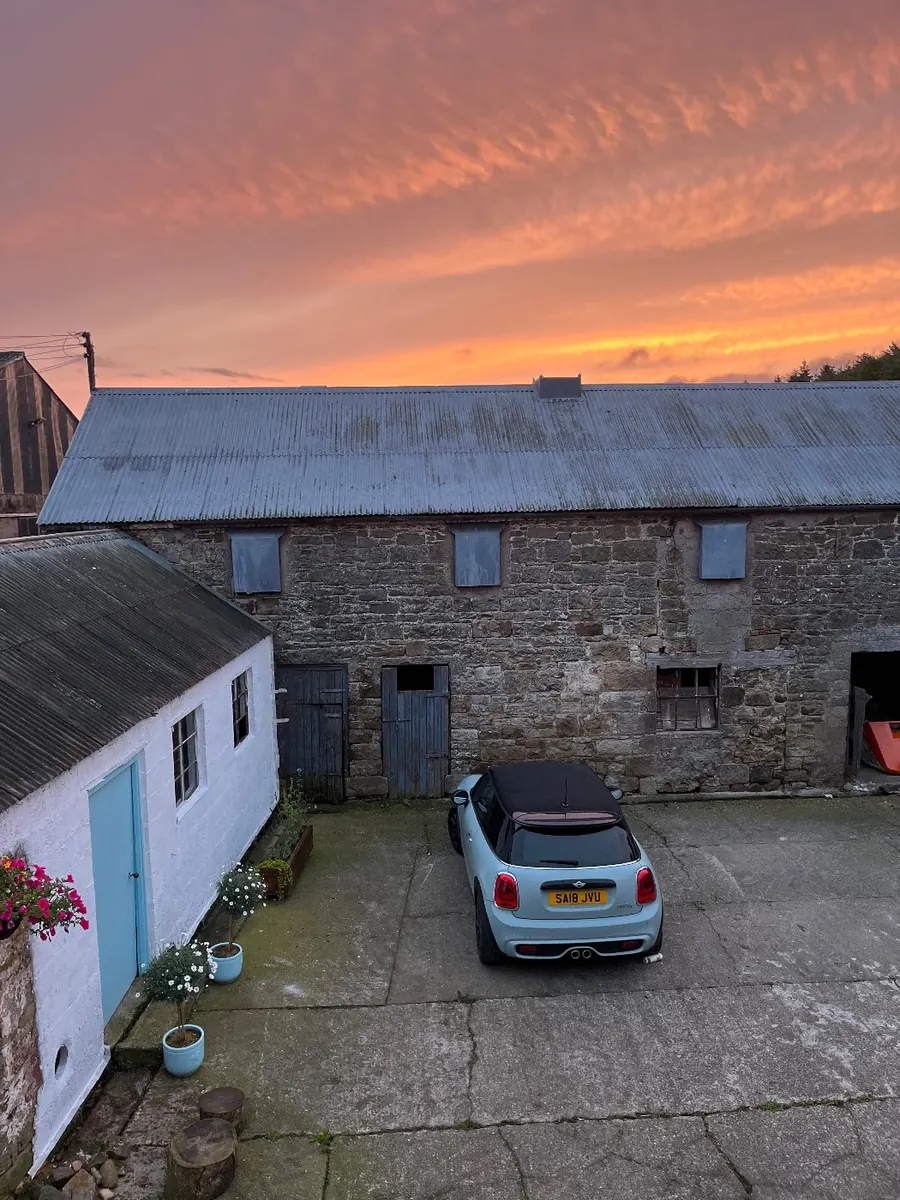 The painted shed under a pink sunset sky, with the stone barns behind