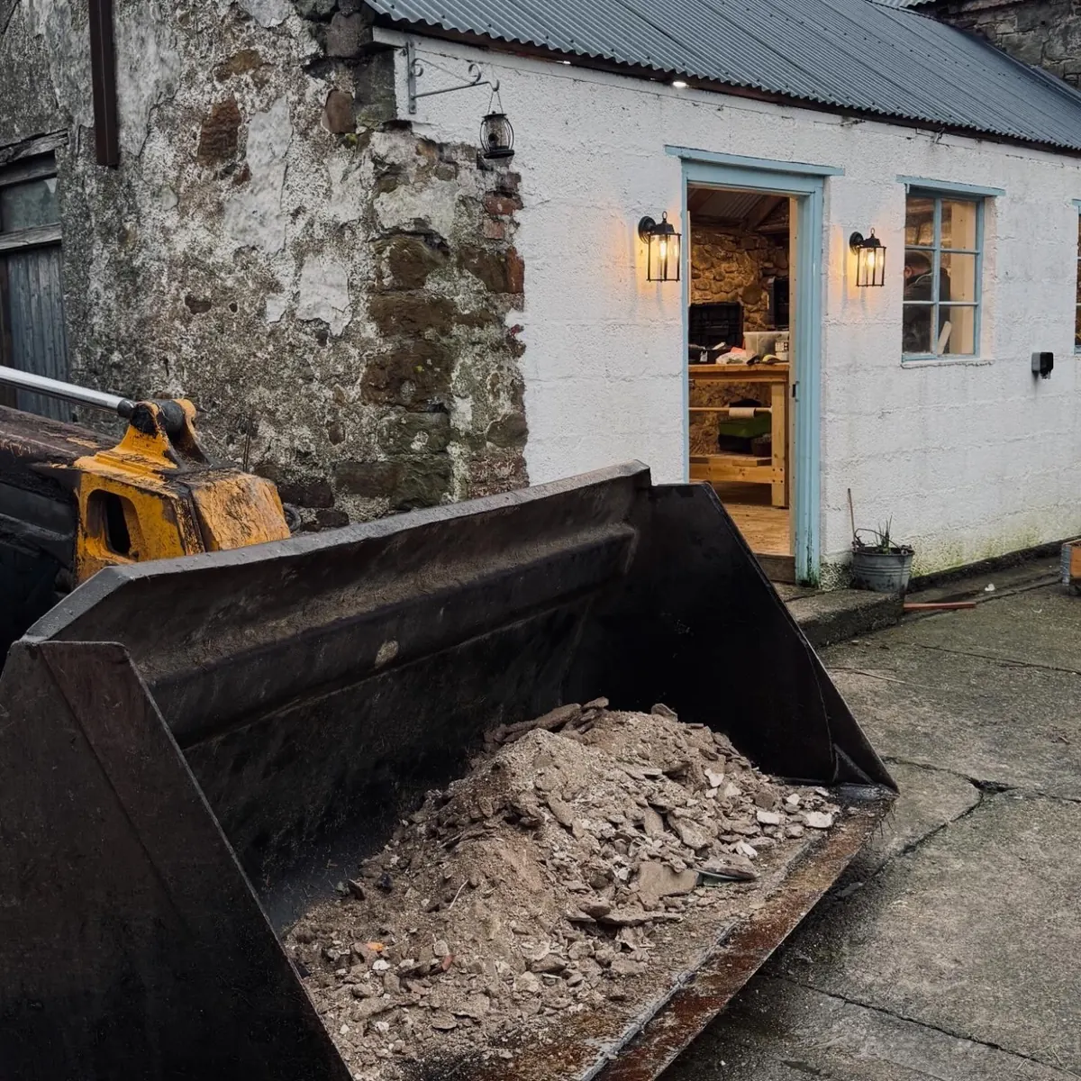 A loader bucket full of rubble outside the lit doorway