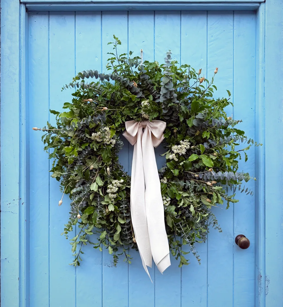 Fresh wreath of eucalyptus and garden foliage with a long ivory silk bow on a pale blue door